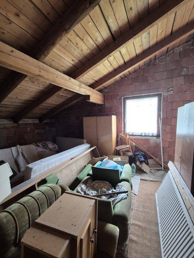 Geräumiger Dachboden mit sichtbaren Holzbalken, Ziegelwänden und einem Fenster für Tageslicht.