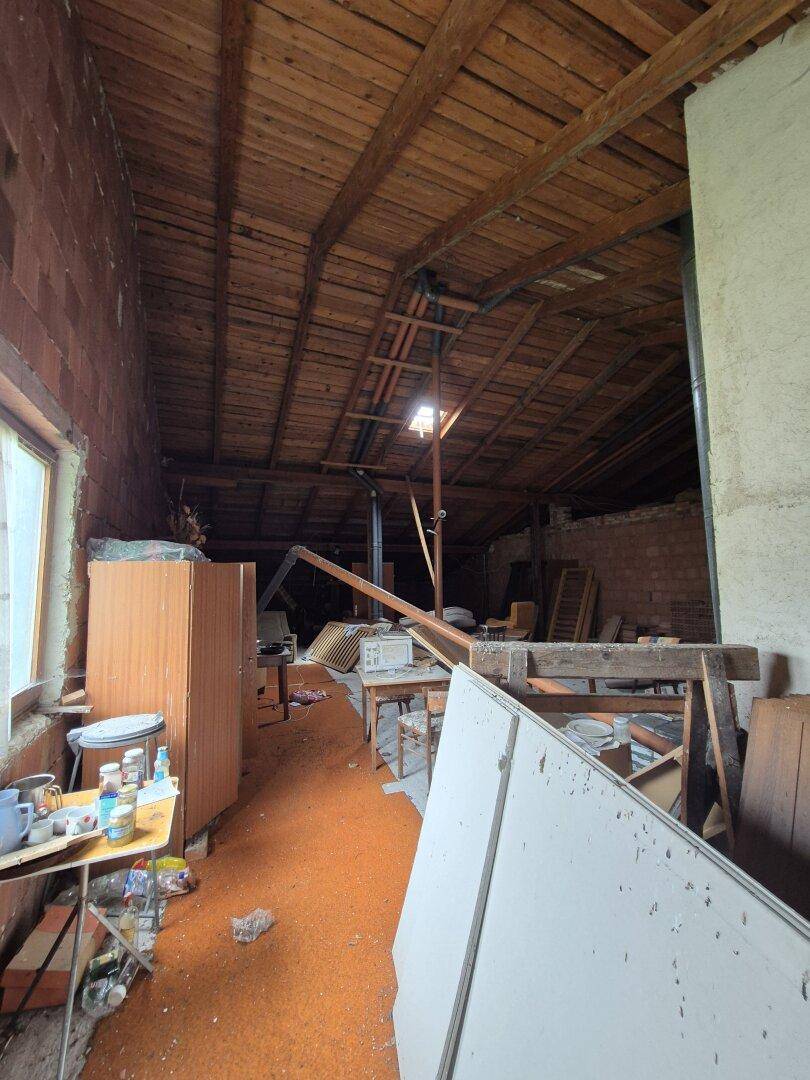 Weiterer Blick auf den Dachboden mit Holzbalken, Ziegelwänden und einem orangefarbenen Teppichboden.