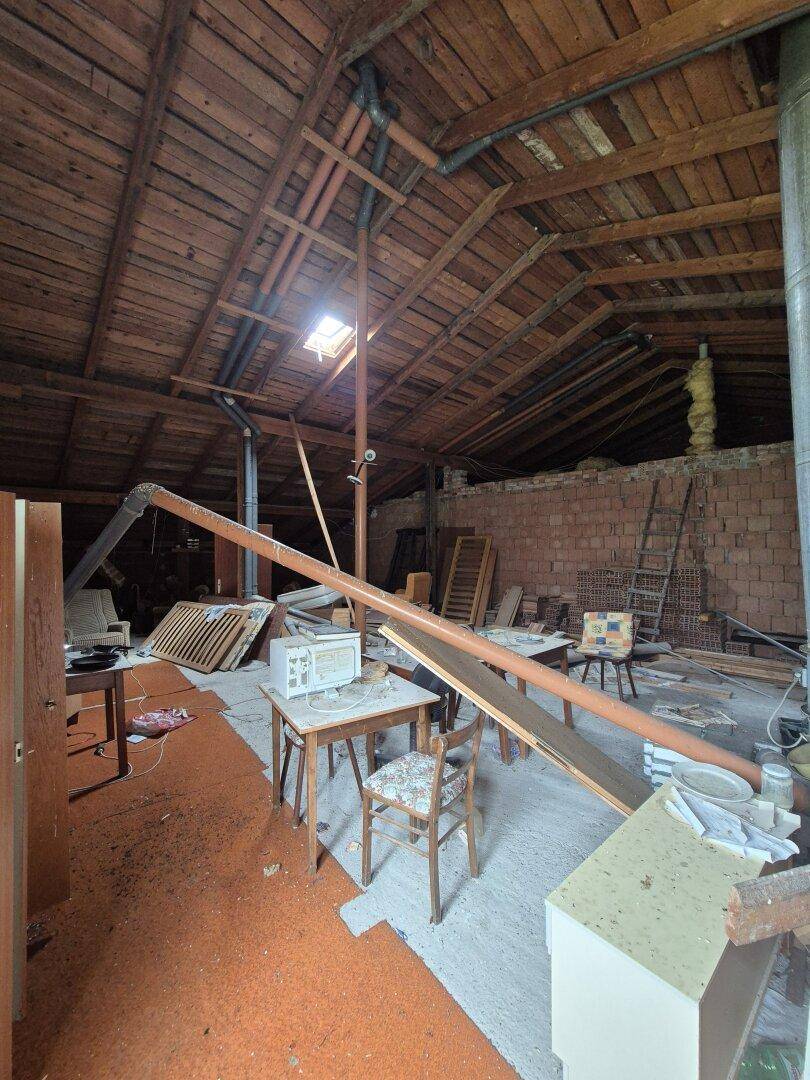 Großer Dachboden mit sichtbaren Holzbalken, Ziegelwänden, Dachfenster und sichtbaren Rohren.