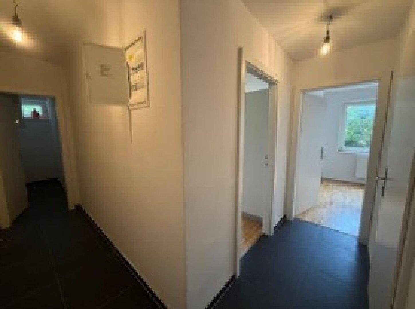 Heller Flur mit dunklem Fliesenboden und Zugang zu verschiedenen Räumen im Inneren des Hauses.