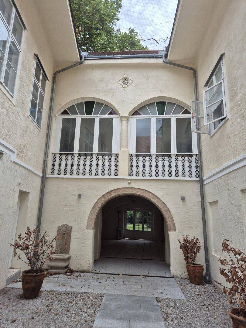 Historischer Innenhof mit gewölbtem Durchgang und dekorativem Balkon im Obergeschoss.