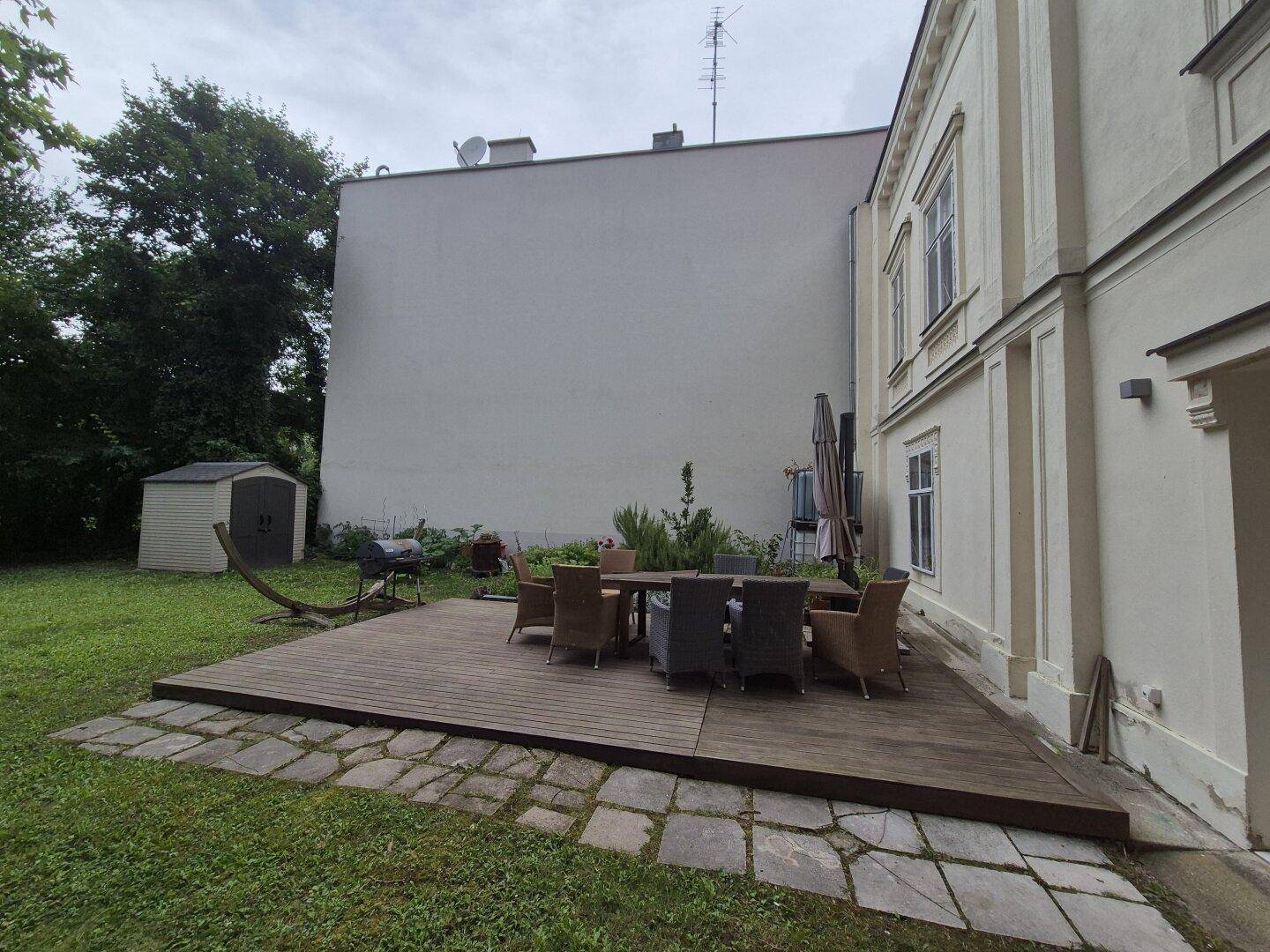 Gepflegter Gartenbereich mit Holzterrasse, Sitzgruppe und Gartenhaus im Hintergrund.