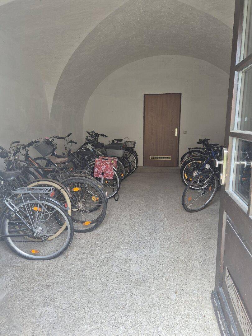 Gewölbter Fahrradraum mit zahlreichen Fahrrädern und einer Holztür im Hintergrund, ideal für Bewohner.