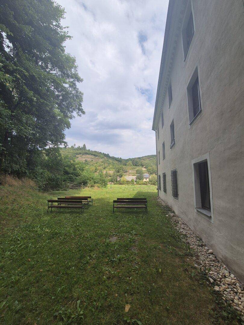 Grüne Wiese mit Holzbänken neben dem Gebäude, bietet einen ruhigen Blick auf die umliegende Hügellandschaft.