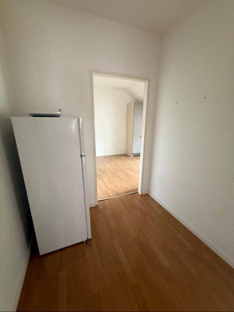 Schmaler Flur mit Laminatboden und einem Kühlschrank, der zu einem weiteren Zimmer führt.