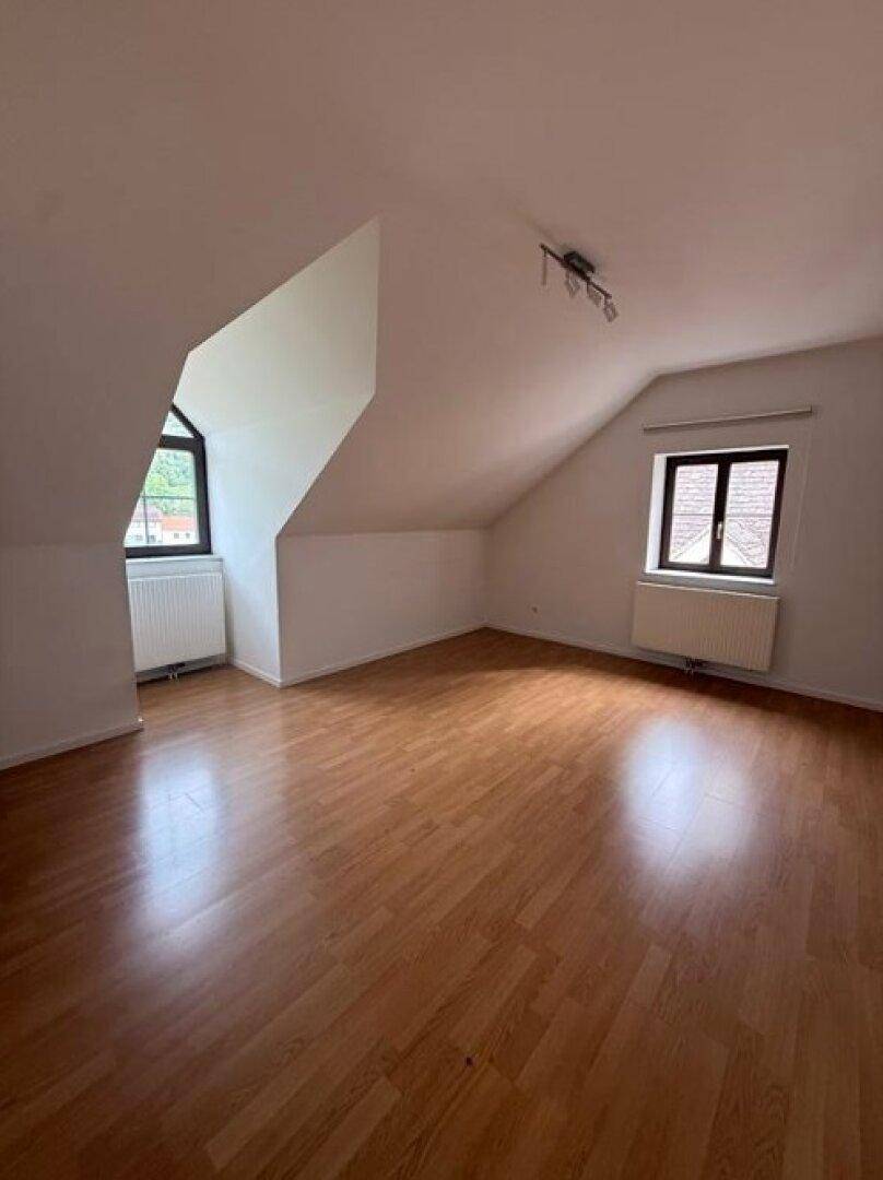 Helles Zimmer im Dachgeschoss mit schrägen Wänden, Laminatboden und zwei Fenstern, bereit zur Einrichtung.