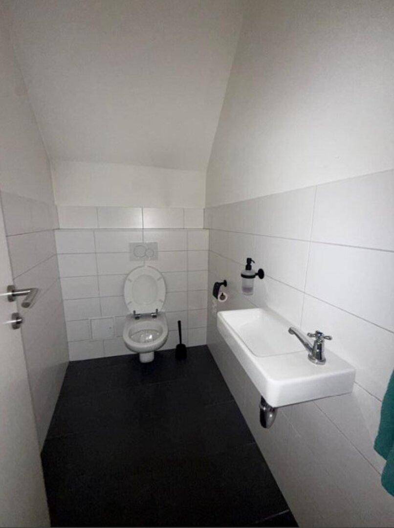 Modernes Gäste-WC mit weißen Fliesen, schwarzem Boden und einem wandmontierten Waschbecken.