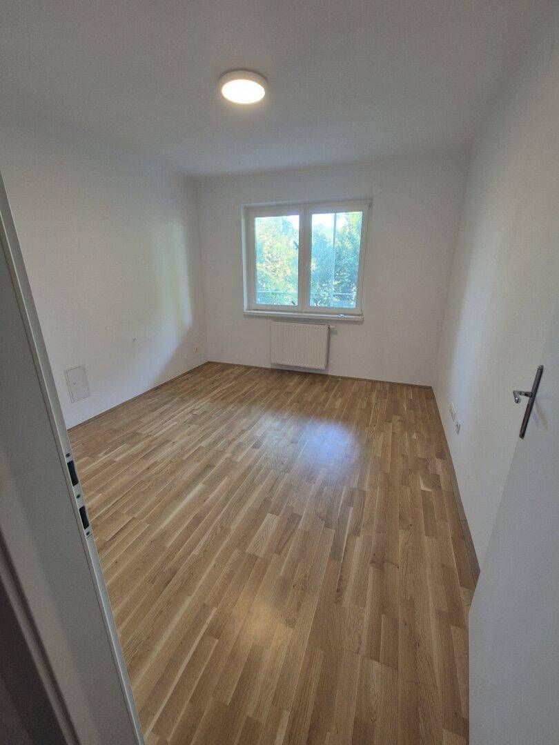 Helles Zimmer mit Holzboden und Fenster, das viel natürliches Licht hereinlässt.