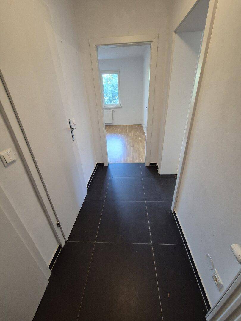 Heller Flur mit dunklen Fliesen, der zu weiteren Zimmern führt.