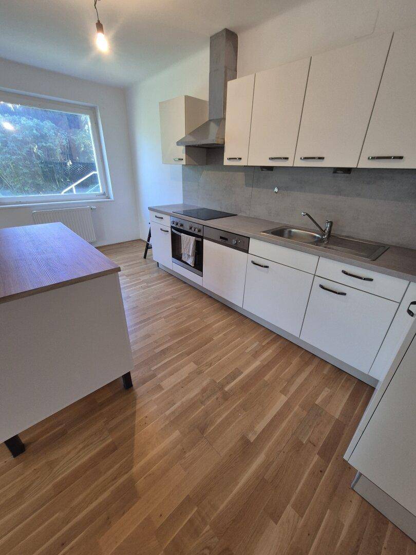 Moderne Einbauküche mit weißen Schränken, Kochfeld und Dunstabzugshaube.