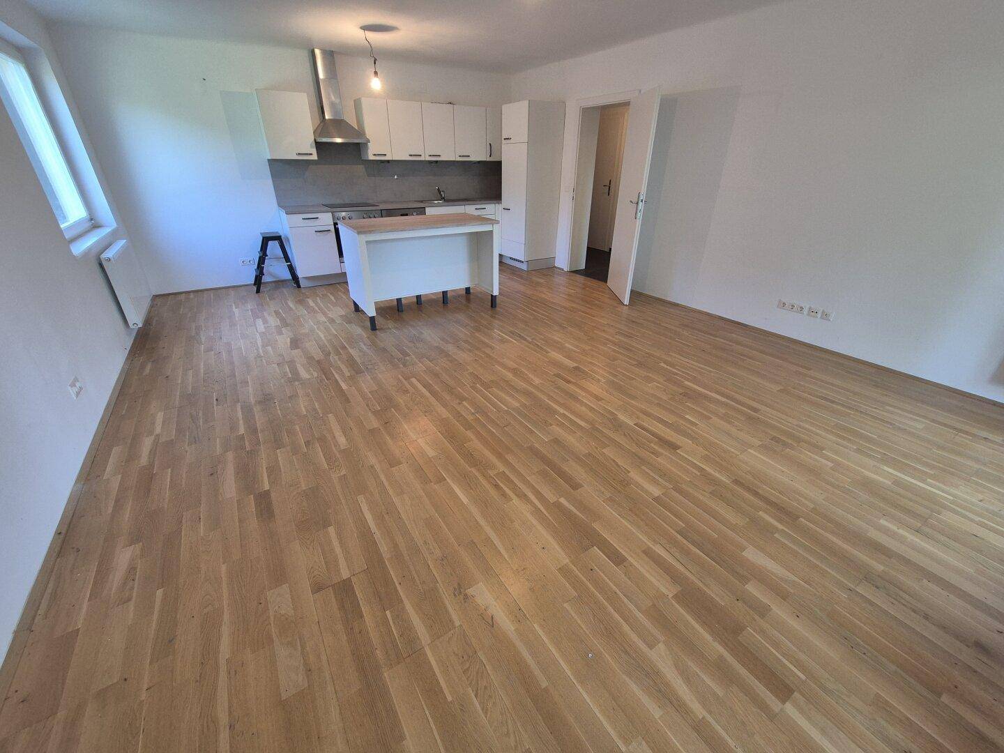 Offener Wohnbereich mit integrierter Küche, Holzboden und viel Tageslicht.