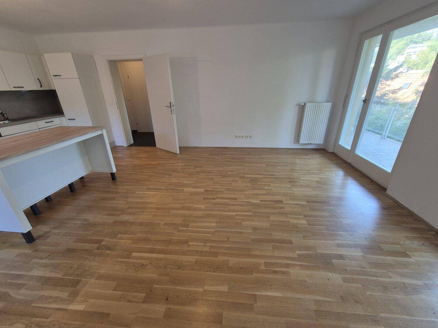 Geräumiger offener Wohnbereich mit Holzboden, Kücheninsel und Zugang zu einem Balkon oder Garten.