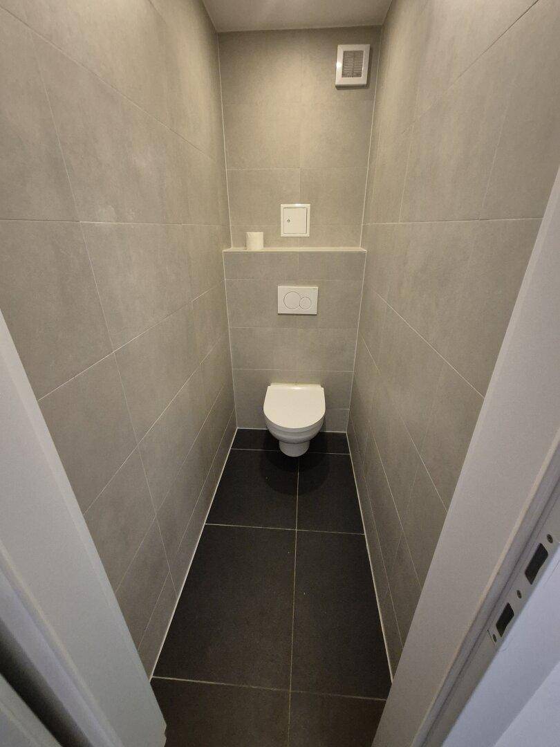 Kleines Gäste-WC mit wandhängender Toilette und modernen grauen Fliesen.