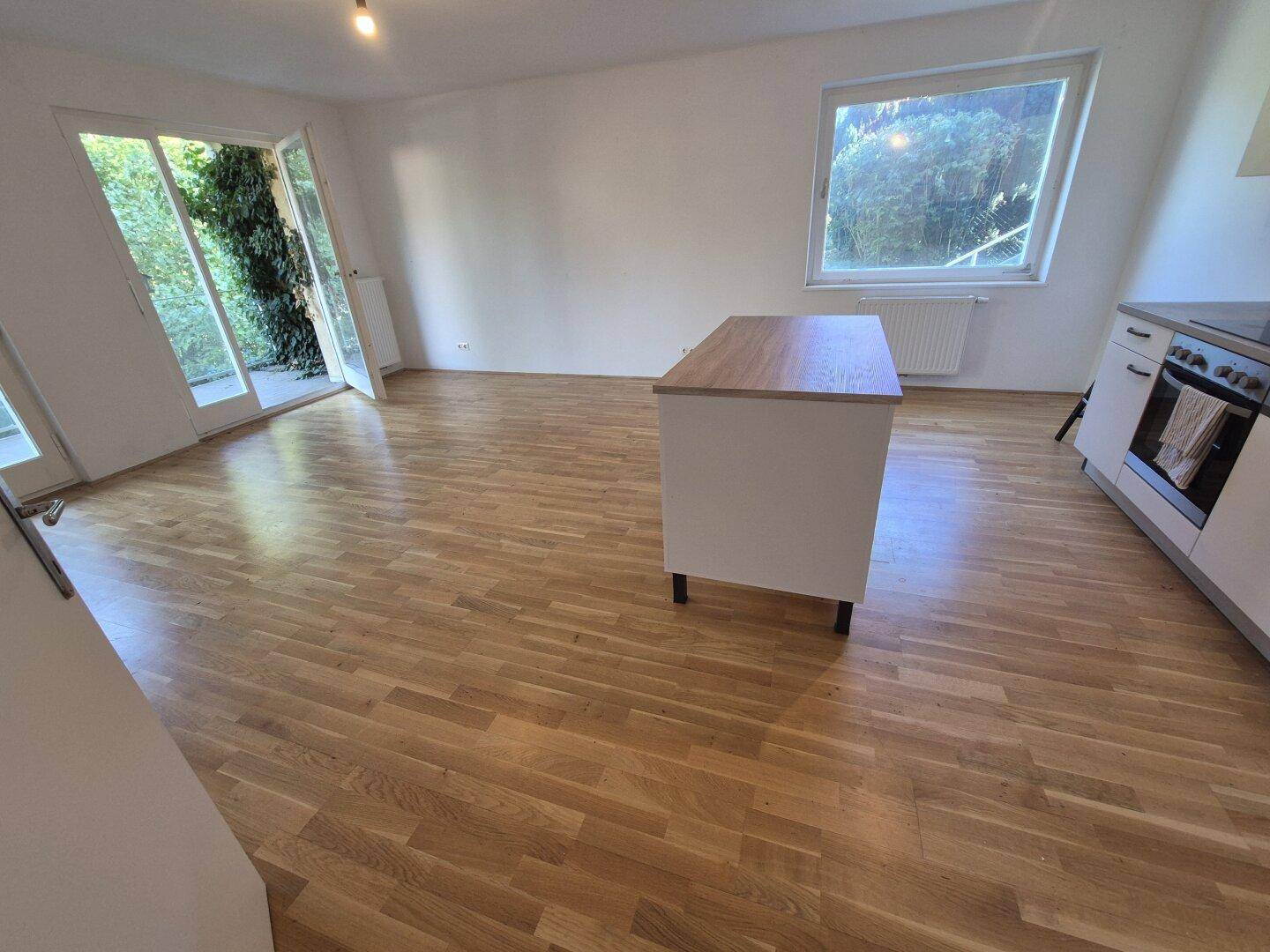 Heller offener Wohnbereich mit Holzboden, Kücheninsel und Zugang zum Außenbereich.