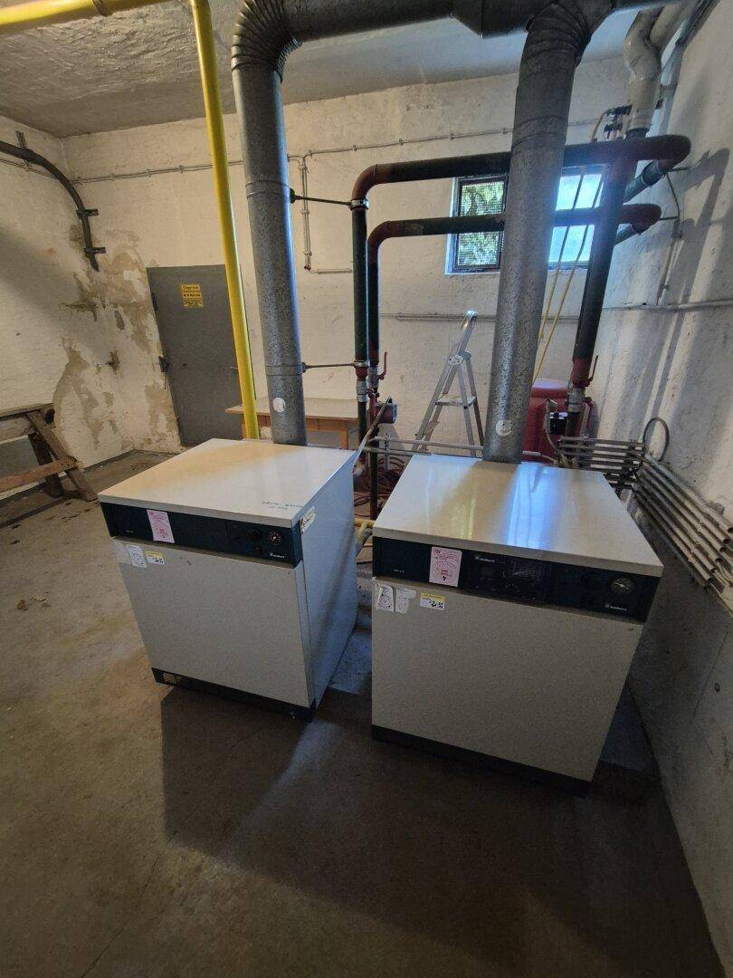 Heizungsraum im Keller mit zwei Heizkesseln und sichtbaren Rohren.