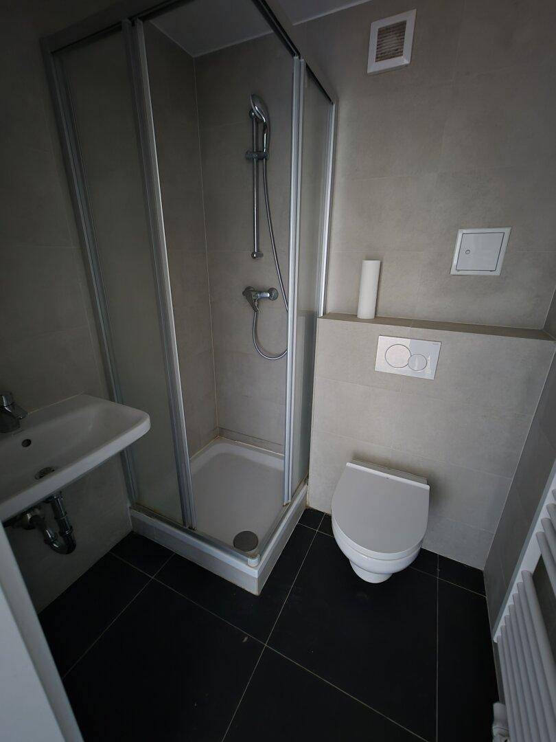 Modernes Badezimmer mit Dusche, wandhängendem WC und dunklen Bodenfliesen.
