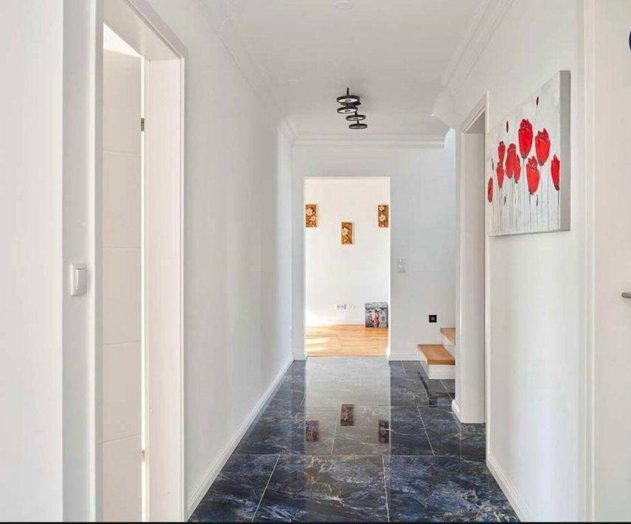 Heller Flur mit glänzenden Fliesen, weiß gestrichenen Wänden und Zugang zu weiteren Räumen.