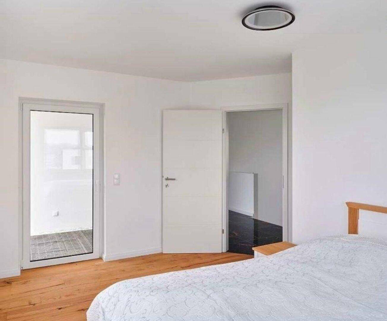 Helles Schlafzimmer mit Holzboden und Zugang zu einem Balkon oder einer Terrasse.