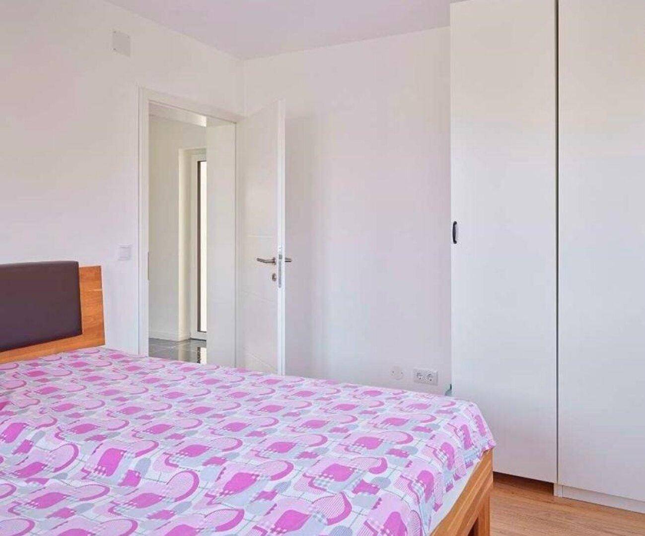 Schlafzimmer mit Holzboden, weißem Kleiderschrank und Zugang zu einem weiteren Raum.