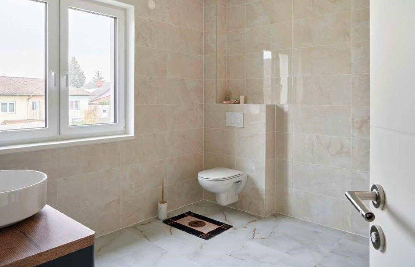 Helles Badezimmer mit Fenster, wandhängendem WC und beigefarbenen Fliesen.