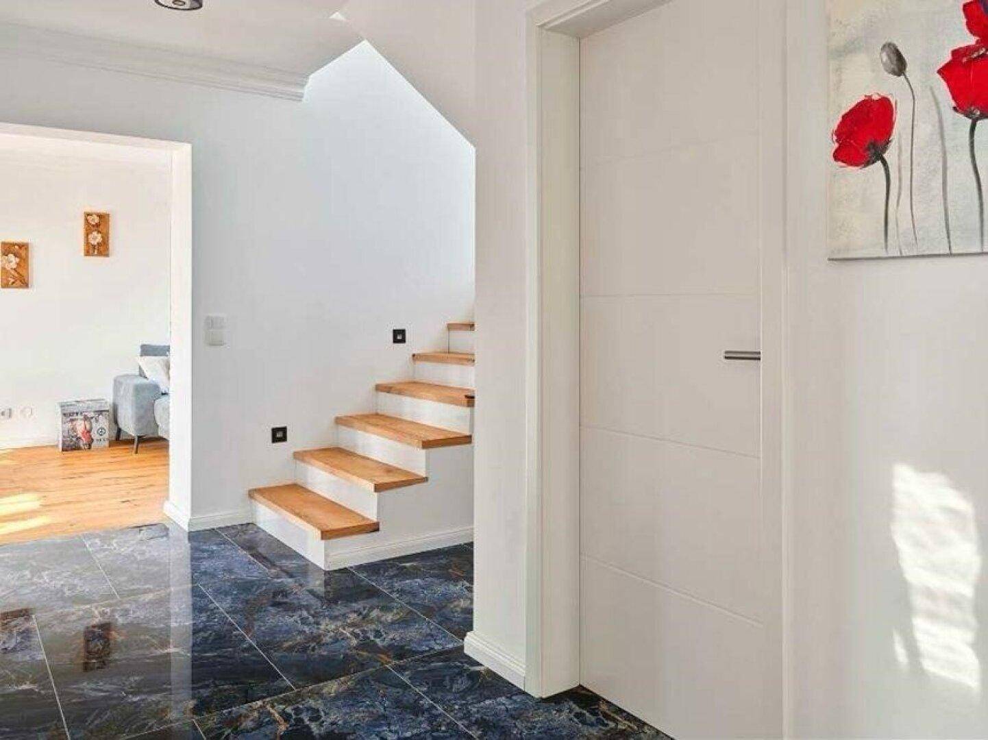 Heller Eingangsbereich mit Holztreppe, dunklen Fliesen und moderner Wanddekoration.