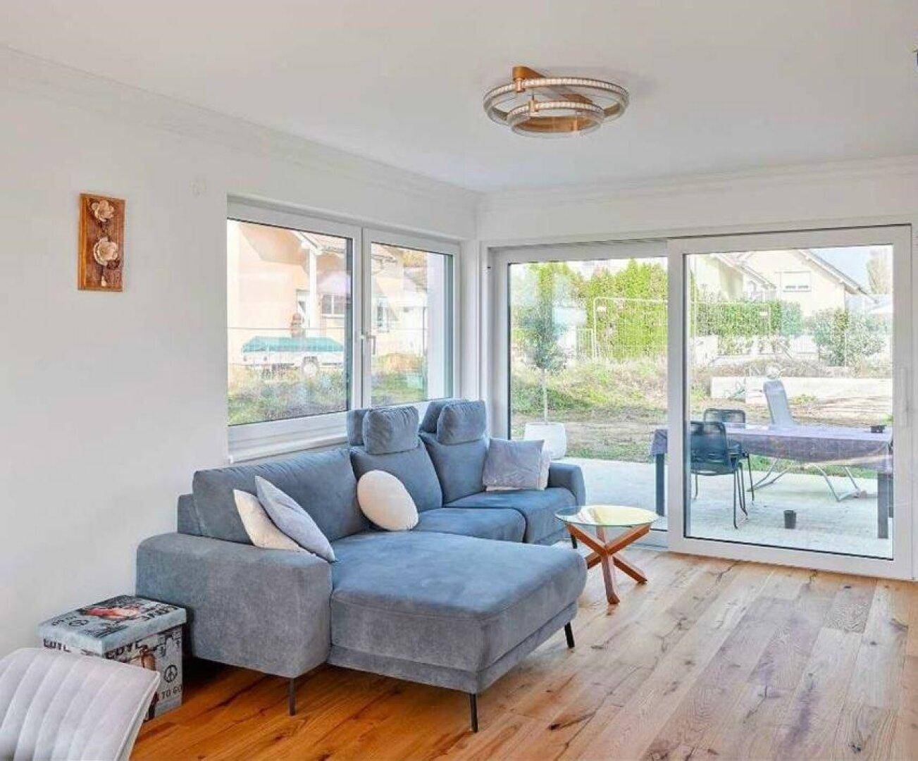 Gemütliches Wohnzimmer mit blauer Eckcouch, Holzboden und Zugang zur Terrasse.