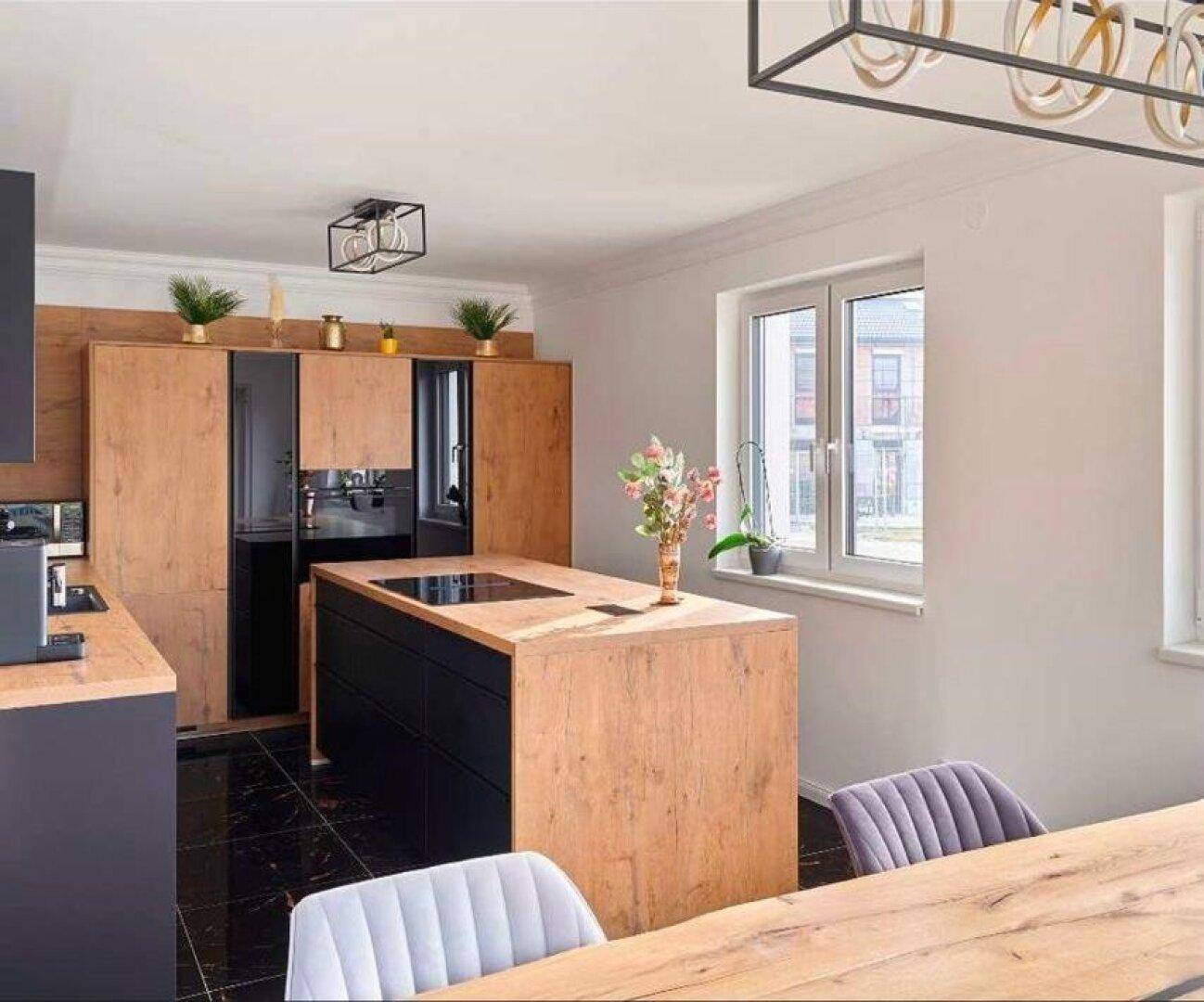 Helle moderne Küche mit Kochinsel, Holzakzenten und Fenster mit Blick nach draußen.