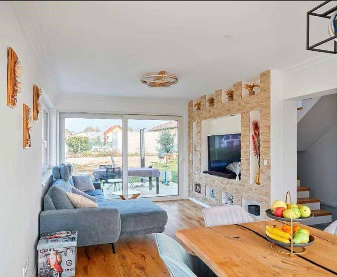 Offener Wohn- und Essbereich mit Holzboden, moderner Wandgestaltung und Terrassenzugang.