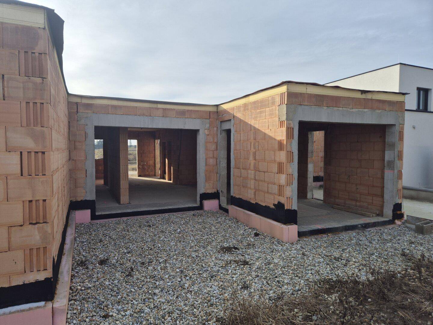 Außenansicht des Rohbaus mit sichtbaren Ziegelwänden und Schotterboden.