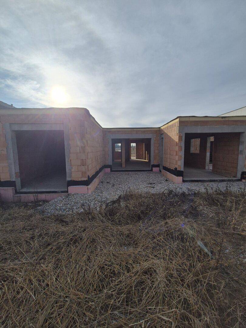 Rohbau eines Einfamilienhauses mit Ziegelwänden unter sonnigem Himmel.