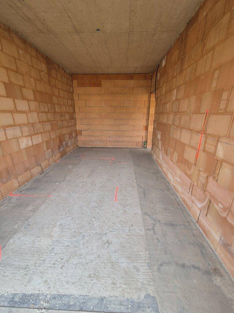 Innenansicht eines Raumes im Rohbau mit Ziegelwänden und Betonboden.
