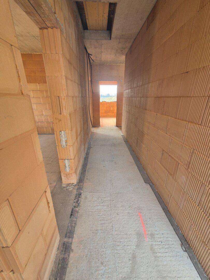 Langer Flur im Rohbau mit Ziegelwänden und Blick ins Freie am Ende.