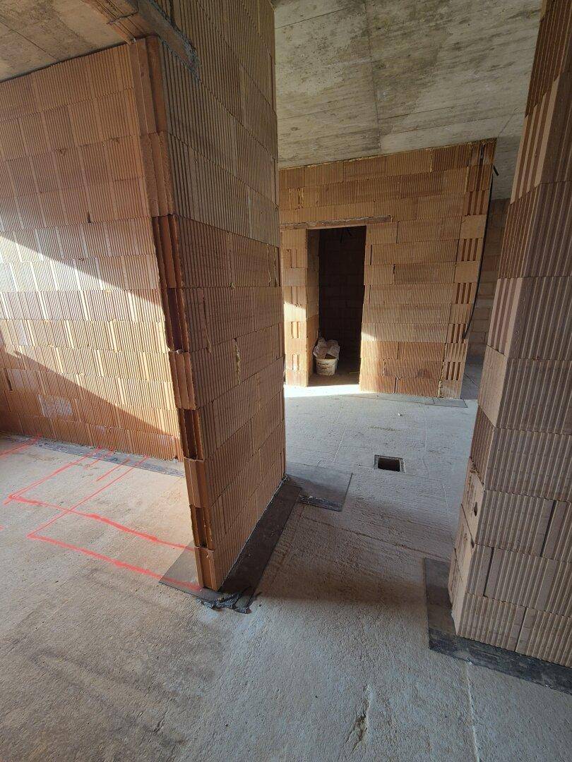 Innenbereich im Rohbau mit mehreren Türöffnungen und sichtbaren Ziegelwänden.