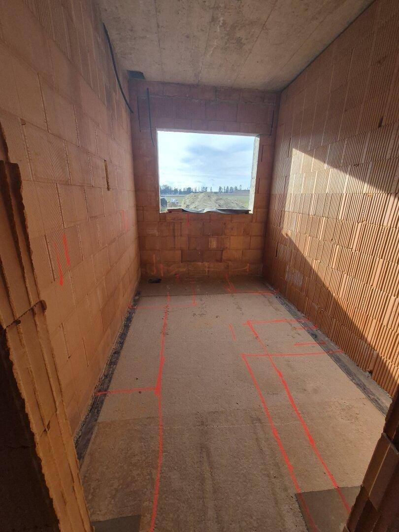 Rohbauzimmer mit Ziegelwänden, Betonboden und einem Fenster, das viel Licht hereinlässt.