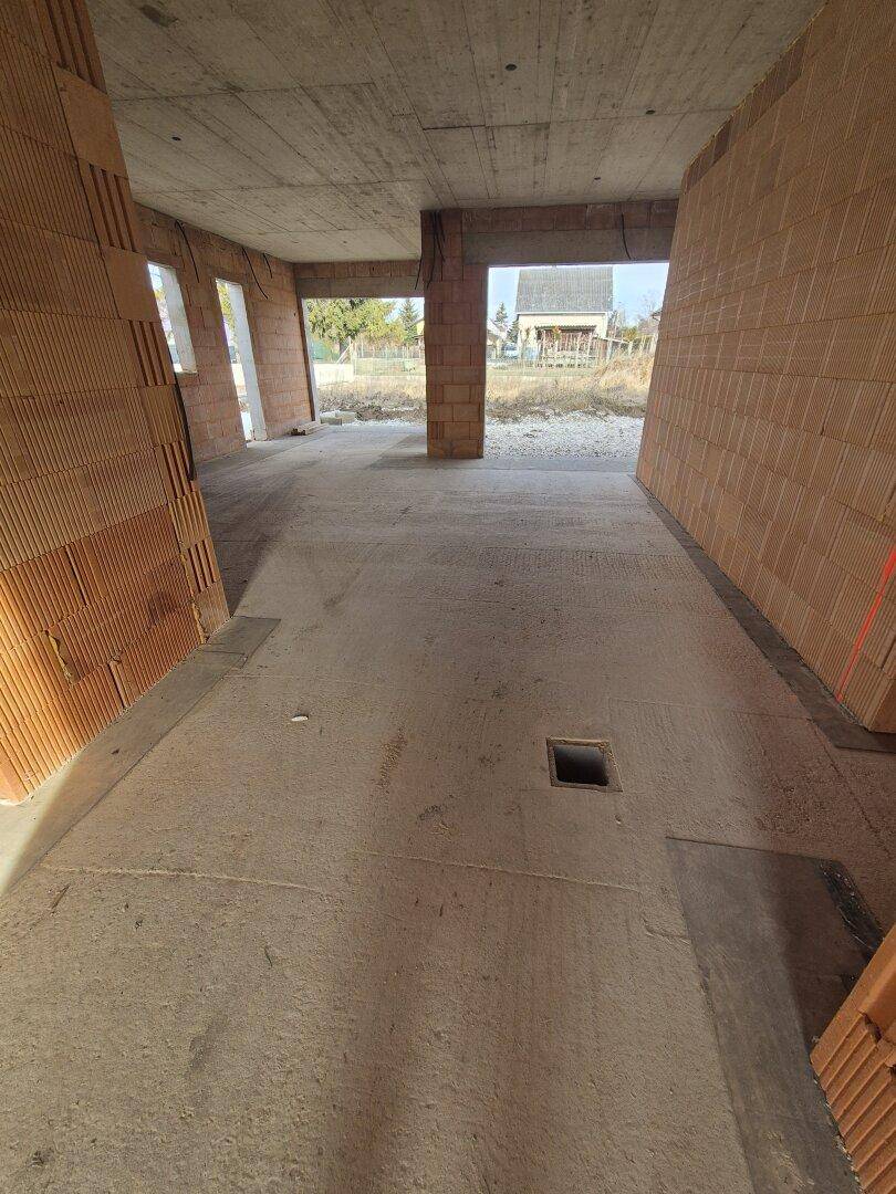 Großer offener Bereich im Rohbau mit Betonboden und Blick nach draußen.