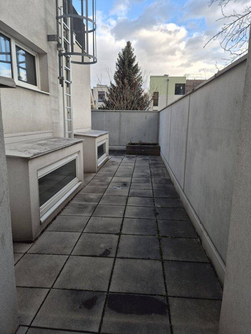 Schmaler Außenbereich mit Fliesenboden und einer Metallleiter, der zusätzlichen Platz im Freien bietet.