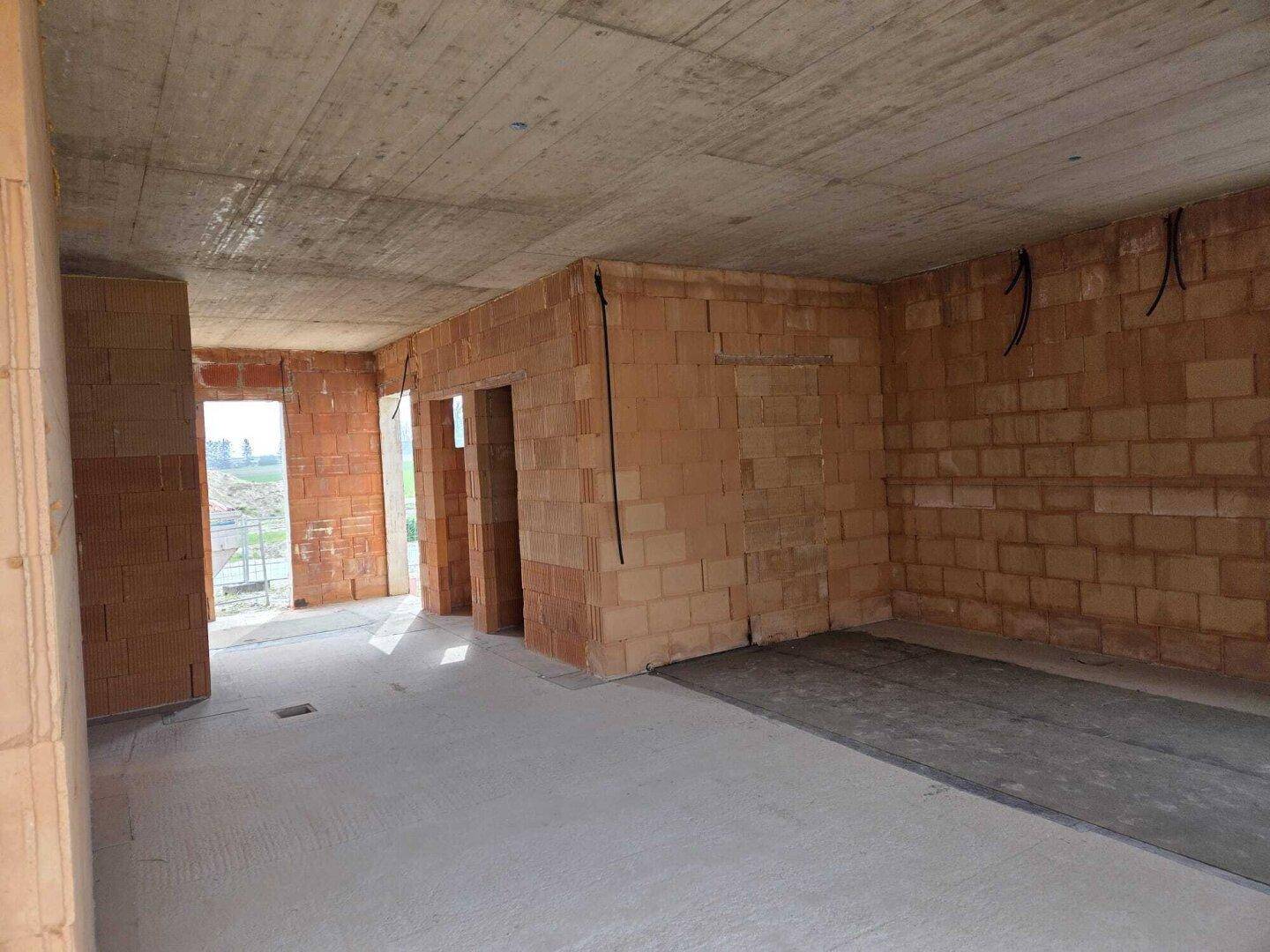 Großer offener Raum im Rohbau mit Ziegelwänden und Betonoberflächen, bereit für den Ausbau.