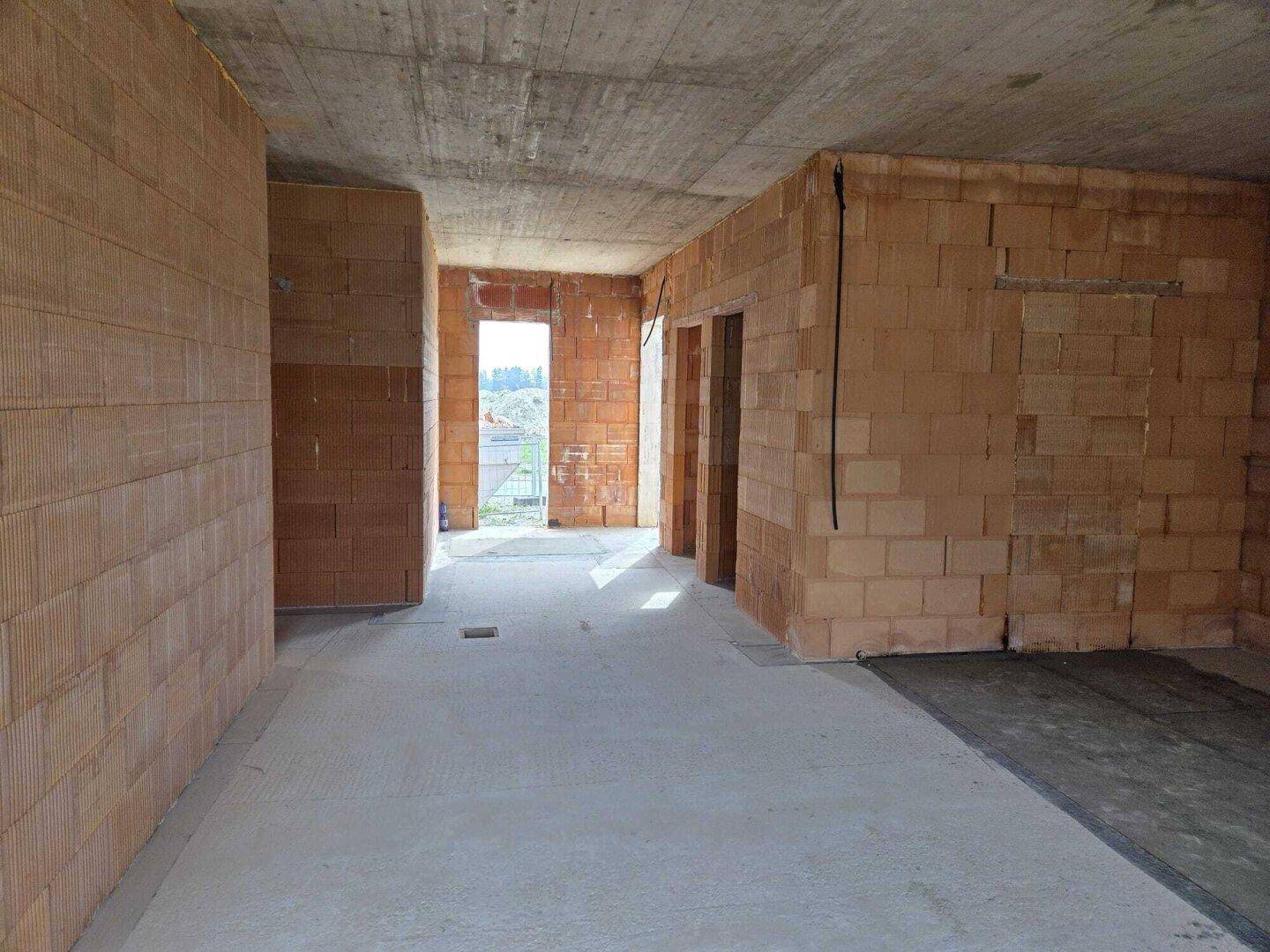 Weitläufiger Innenraum im Rohbau mit unverputzten Ziegelwänden und Betonboden.