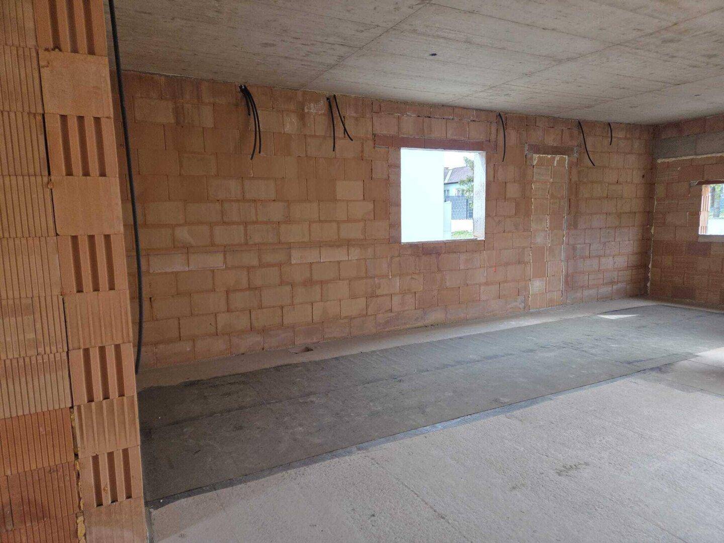 Innenraum im Rohbau mit Ziegelwänden, Betonboden und Fensteröffnungen, bereit für den Ausbau.