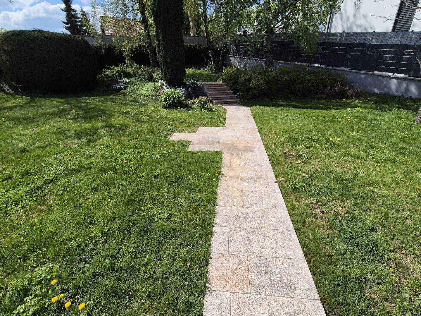 Geschwungener Gartenweg aus Steinplatten führt durch den grünen Rasen zu einer Treppe.