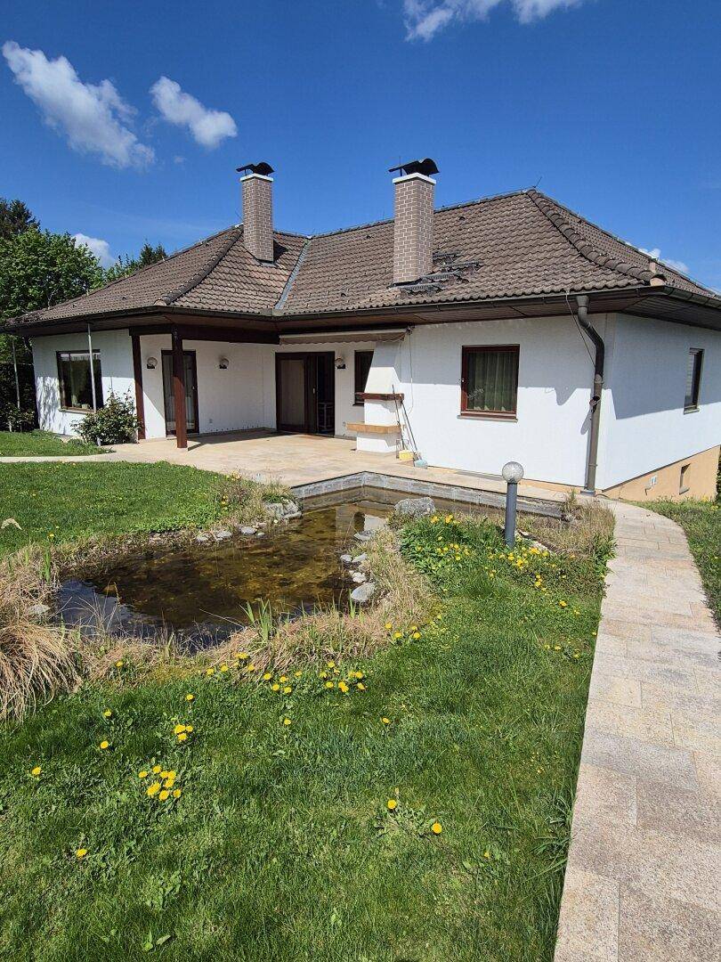 Rückansicht des Hauses mit Teich im Garten, gepflastertem Weg und braunem Ziegeldach.