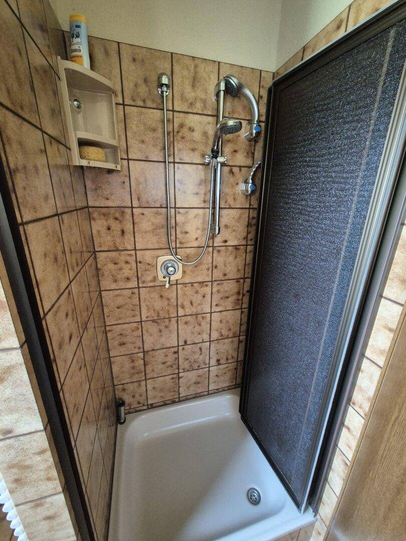 Duschbereich mit braunen Fliesen und Duschkabine im Badezimmer.