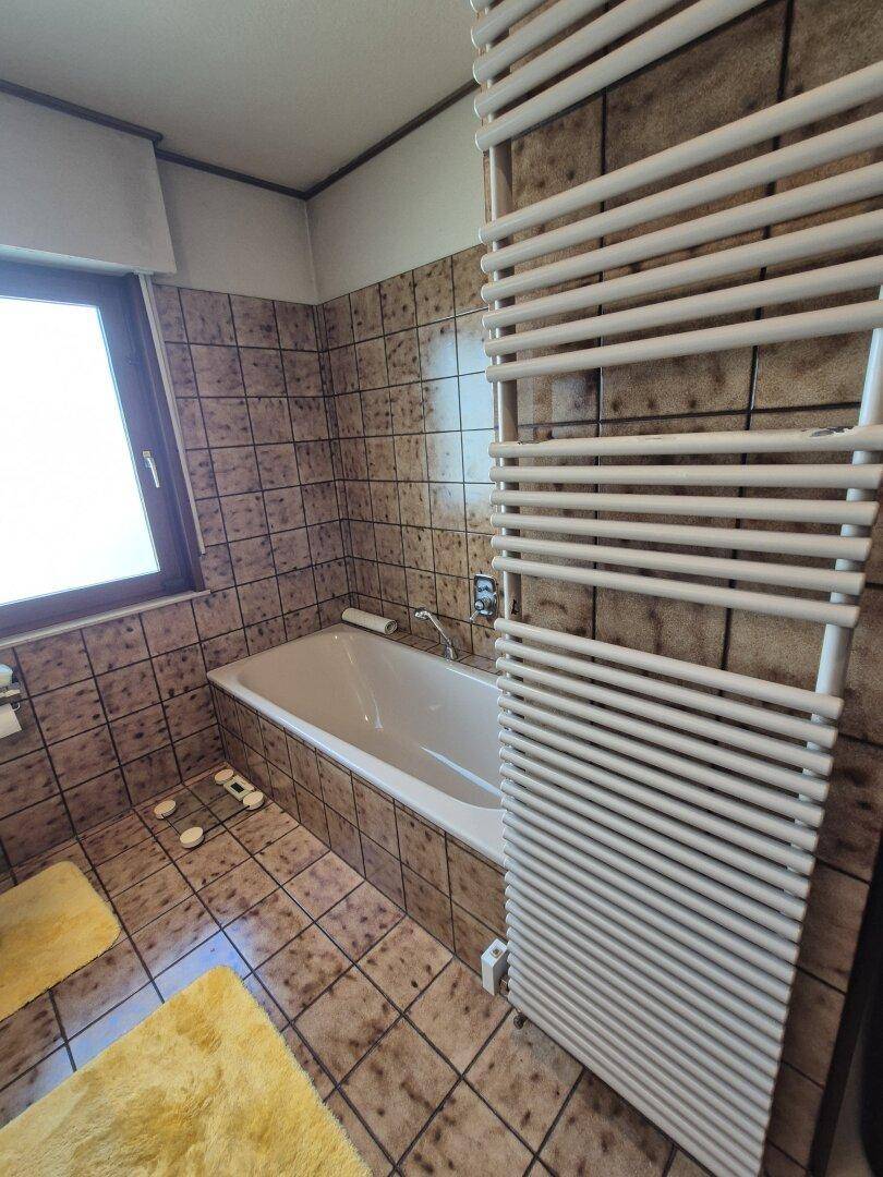 Badewanne mit braunen Fliesen und modernem Handtuchheizkörper im Badezimmer.
