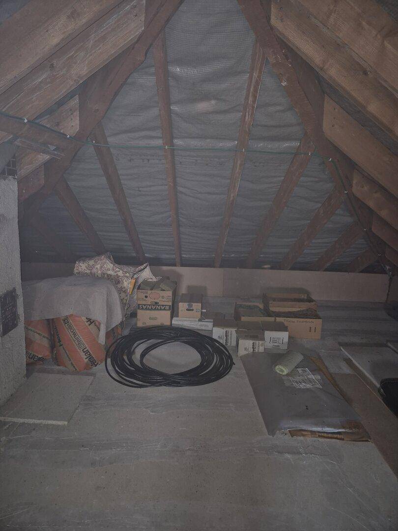 Unausgebauter Dachboden mit sichtbaren Holzbalken und gelagerten Gegenständen, bietet Stauraum.
