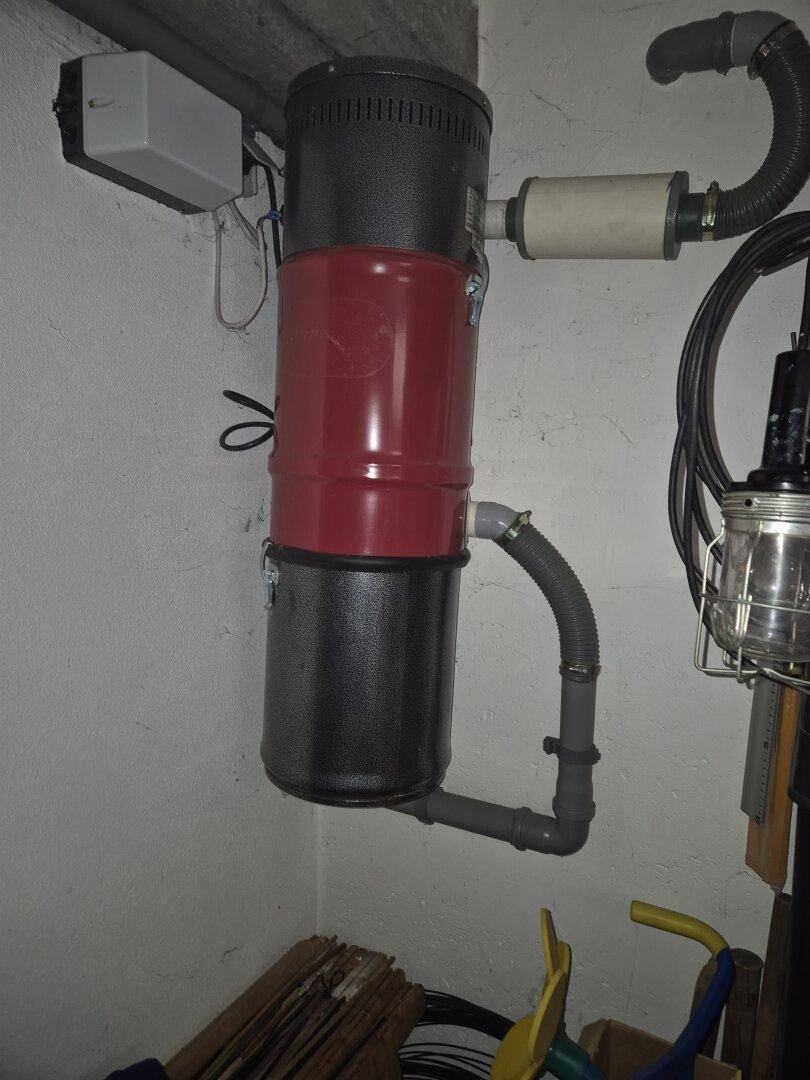 Zentralstaubsaugeranlage an der Wand eines Technikraums montiert, mit sichtbaren Leitungen.