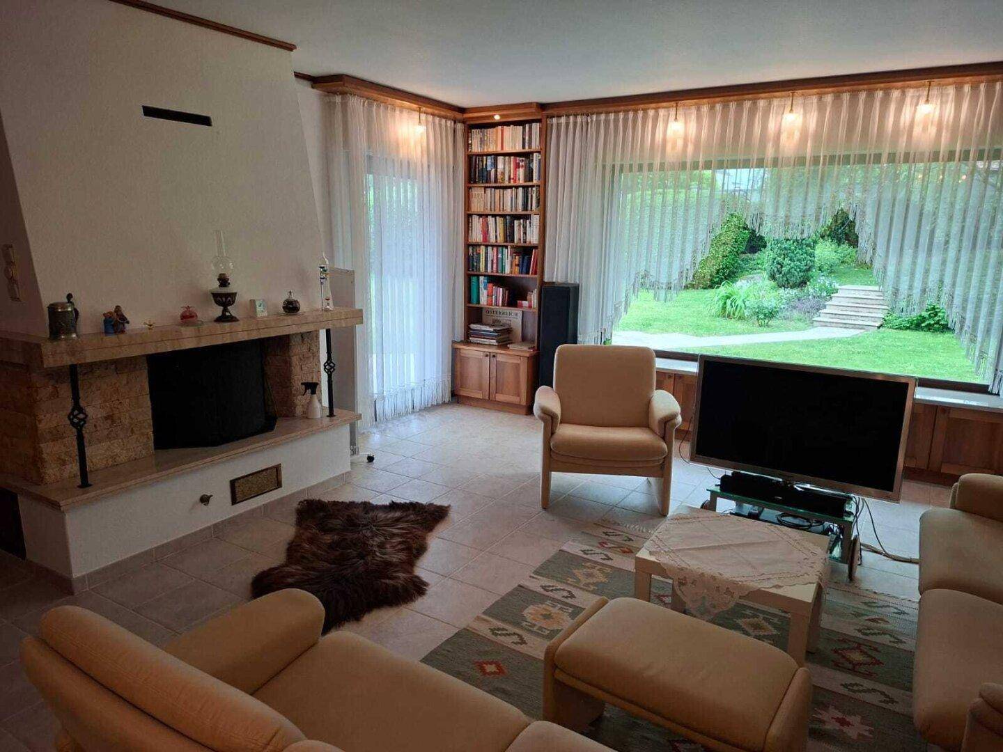 Helles Wohnzimmer mit großem Fenster, Kamin und Bücherregal, bietet viel Platz zum Entspannen.