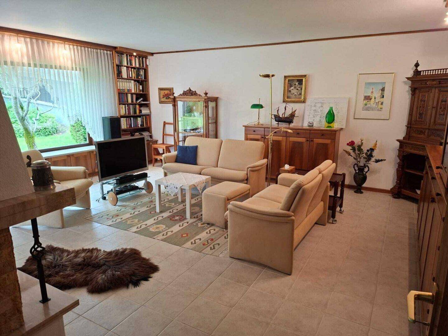Geräumiges Wohnzimmer mit beigen Sofas, Kamin und Blick in den gepflegten Garten.