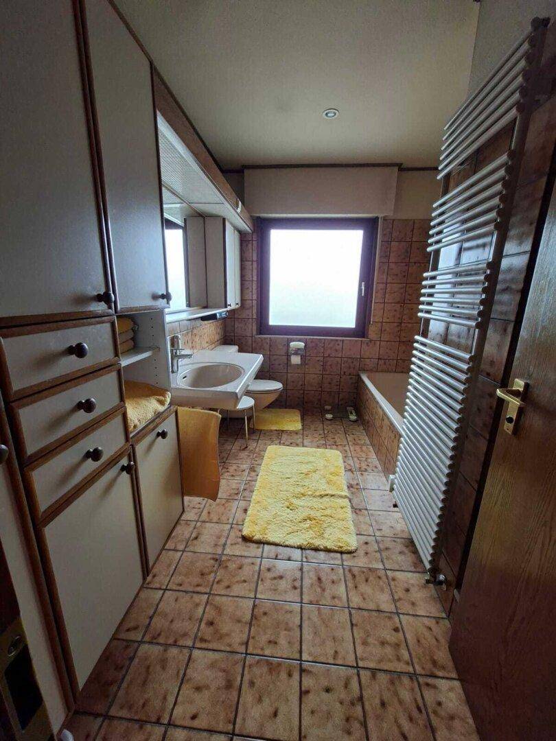 Badezimmer mit Fenster, Badewanne und braunen Fliesen, bietet ausreichend Stauraum.