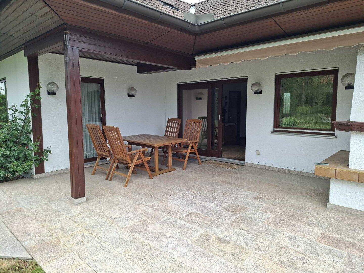 Gemütliche Terrasse mit Holztisch und Stühlen, überdachtem Bereich und Zugang zum Garten.
