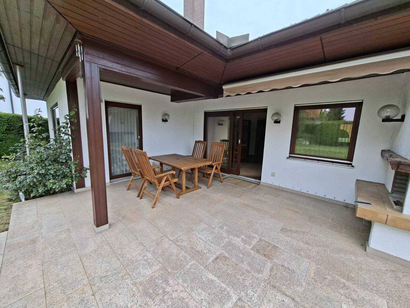 Überdachte Terrasse mit Holztischgruppe und gefliestem Boden, ideal für Mahlzeiten im Freien.